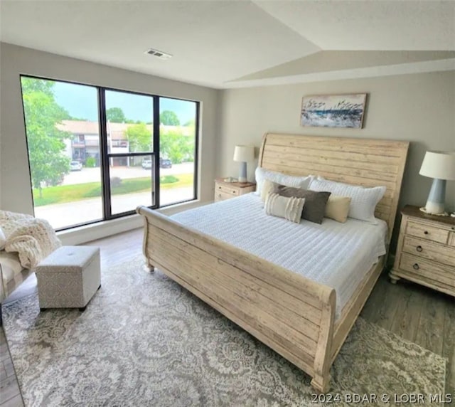 bedroom featuring dark wood-type flooring, vaulted ceiling, and multiple windows