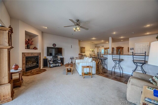 carpeted living room featuring ceiling fan and a tiled fireplace