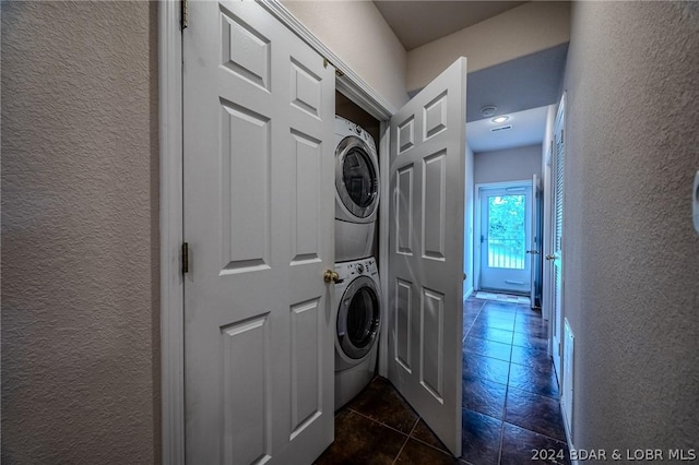 clothes washing area with stacked washer and dryer and dark tile patterned floors