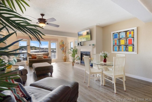 living room featuring ceiling fan, wood-type flooring, a textured ceiling, and a fireplace