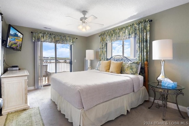 bedroom with ceiling fan, access to outside, light colored carpet, a water view, and a textured ceiling