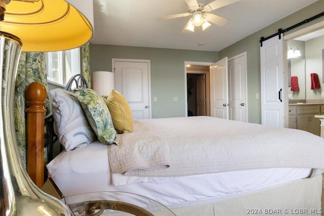 bedroom with ceiling fan, connected bathroom, and a barn door