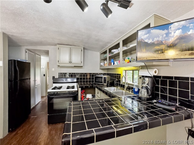 kitchen featuring black refrigerator, gas range, dark wood-type flooring, sink, and tile counters