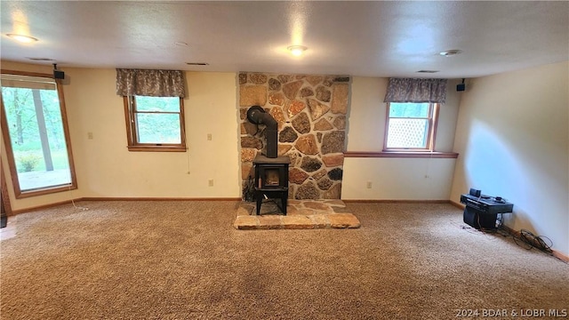 unfurnished living room featuring a wealth of natural light, carpet floors, and a wood stove