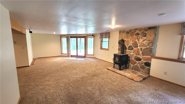 unfurnished living room featuring carpet, a wood stove, and a textured ceiling