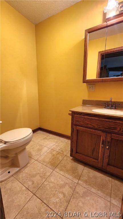 bathroom featuring vanity, toilet, tile patterned flooring, and a textured ceiling