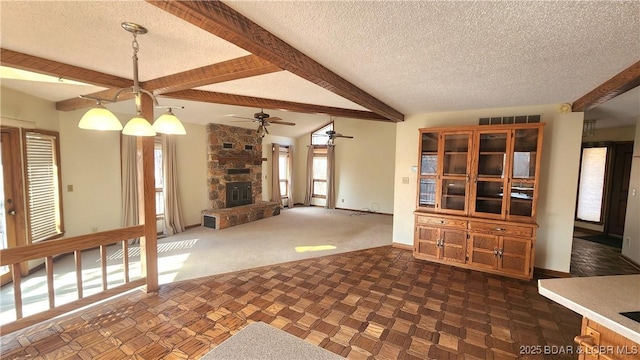 unfurnished living room with a stone fireplace, lofted ceiling with beams, ceiling fan, dark carpet, and a textured ceiling