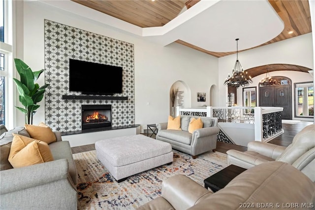 living room featuring wood-type flooring, wood ceiling, a tiled fireplace, and a notable chandelier