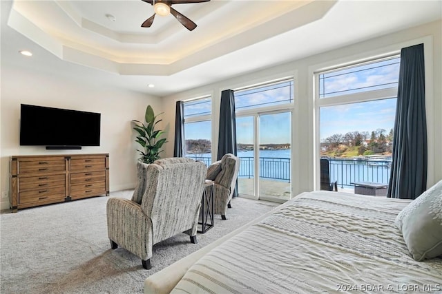 bedroom featuring light carpet, ceiling fan, access to outside, a tray ceiling, and a water view