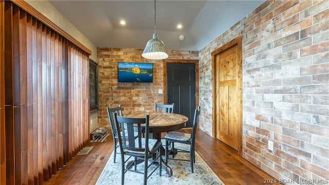 dining space featuring brick wall, dark hardwood / wood-style floors, and vaulted ceiling