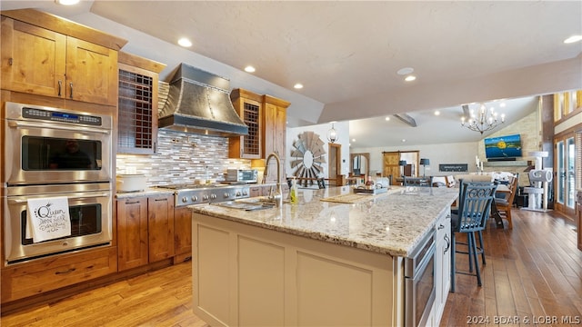 kitchen with light hardwood / wood-style flooring, backsplash, an island with sink, custom exhaust hood, and appliances with stainless steel finishes