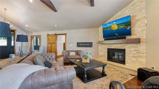 living room with a stone fireplace, lofted ceiling with beams, hardwood / wood-style floors, and a barn door