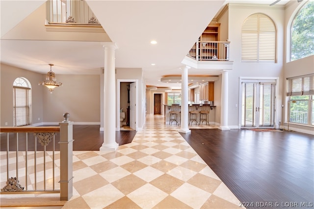 interior space with a chandelier, a towering ceiling, ornate columns, and light wood-type flooring