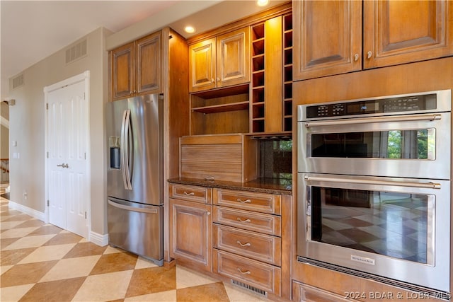 kitchen featuring appliances with stainless steel finishes, light tile patterned floors, and dark stone counters