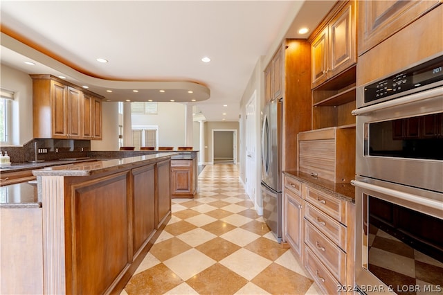 kitchen with light tile patterned floors, kitchen peninsula, dark stone counters, stainless steel appliances, and decorative backsplash