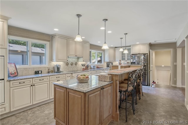 kitchen with backsplash, a kitchen breakfast bar, a kitchen island with sink, light stone countertops, and pendant lighting