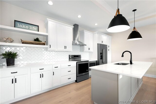 kitchen with pendant lighting, white cabinets, wall chimney exhaust hood, light stone counters, and stainless steel appliances