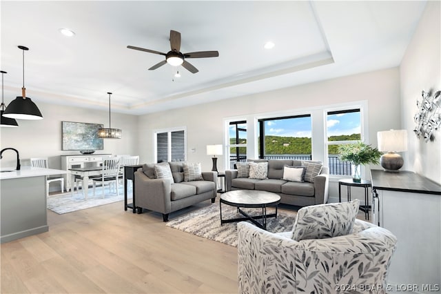 living room featuring a raised ceiling, ceiling fan, and light wood-type flooring