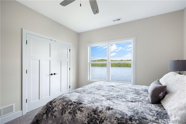 carpeted bedroom with ceiling fan, a closet, and a water view