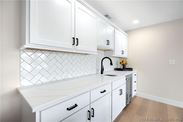 kitchen featuring sink, light hardwood / wood-style flooring, decorative backsplash, light stone counters, and white cabinetry