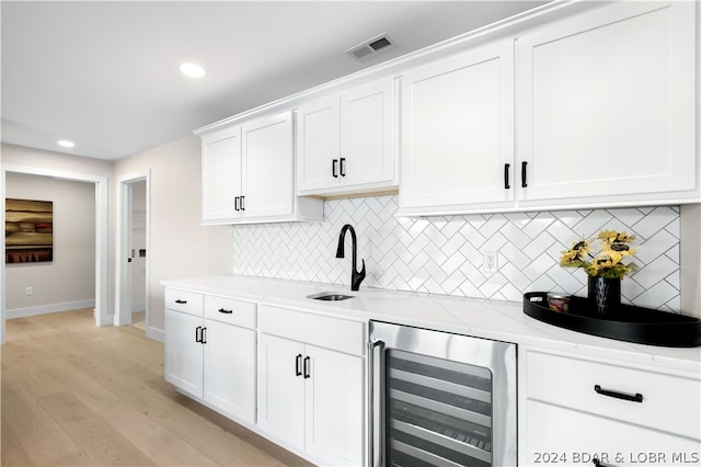 kitchen with light stone countertops, white cabinets, beverage cooler, and light wood-type flooring