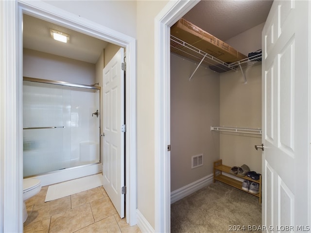 interior space featuring tile patterned flooring, an enclosed shower, and toilet