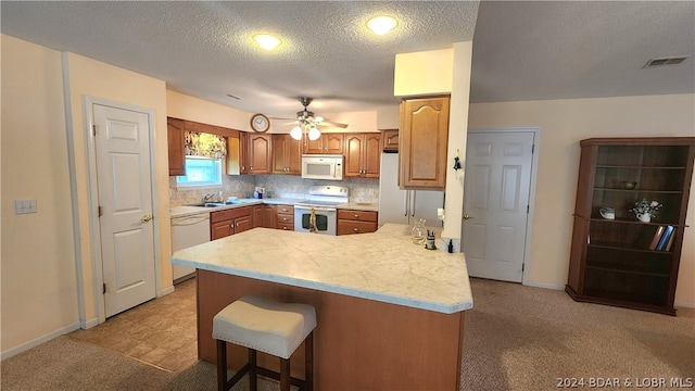 kitchen with sink, white appliances, a breakfast bar area, light carpet, and kitchen peninsula