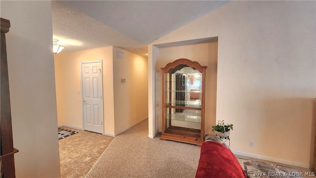 corridor with light carpet, vaulted ceiling, and a textured ceiling