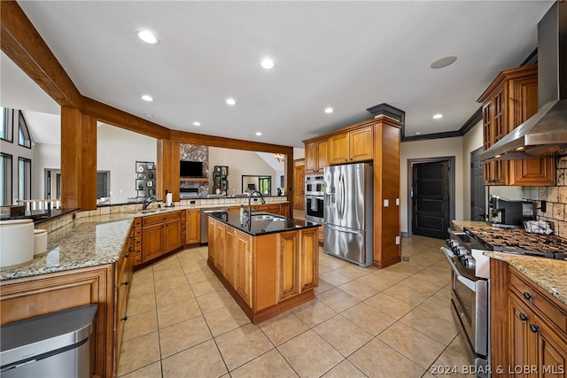 kitchen with dark stone counters, stainless steel appliances, wall chimney exhaust hood, sink, and a center island with sink