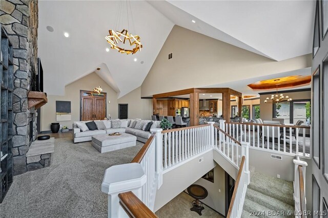 carpeted living room with an inviting chandelier, a stone fireplace, and high vaulted ceiling