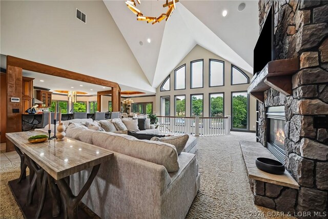 carpeted living room with an inviting chandelier, a stone fireplace, and high vaulted ceiling