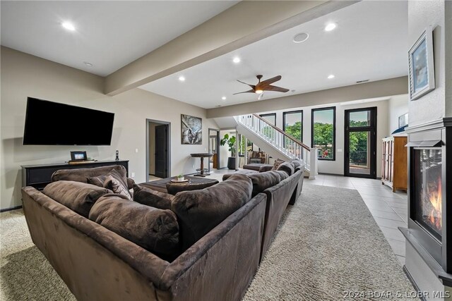 tiled living room featuring a premium fireplace, ceiling fan, and beam ceiling