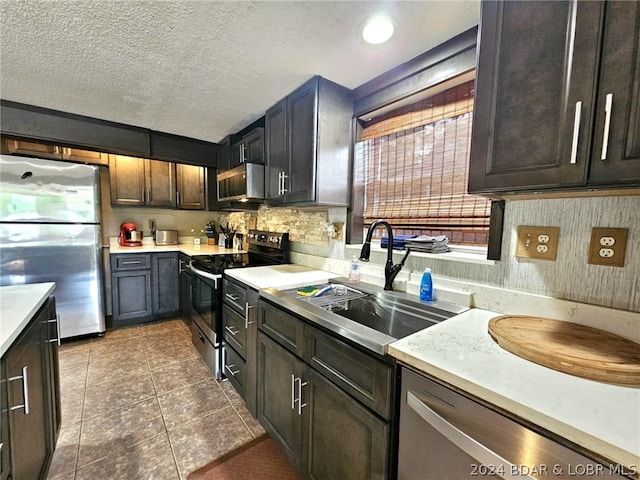 kitchen with sink, dark brown cabinets, stainless steel appliances, a textured ceiling, and dark tile patterned flooring