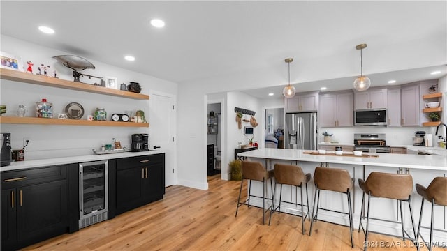 kitchen with a breakfast bar, light wood-type flooring, appliances with stainless steel finishes, pendant lighting, and beverage cooler