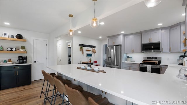 kitchen with pendant lighting, light hardwood / wood-style flooring, gray cabinetry, stainless steel appliances, and a kitchen bar