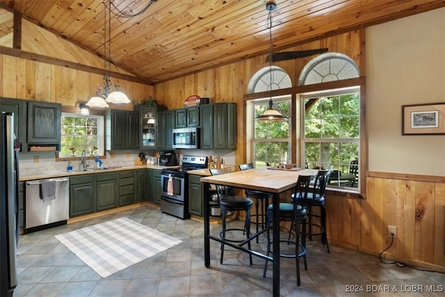 kitchen featuring appliances with stainless steel finishes, wood ceiling, sink, hanging light fixtures, and wood walls