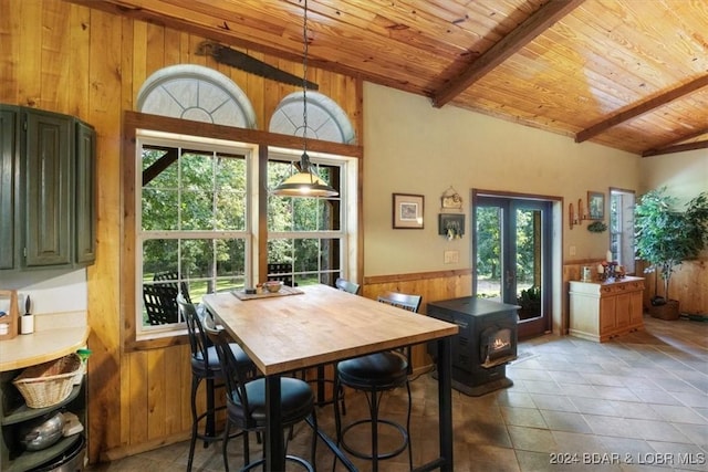 dining area with a wood stove, wooden ceiling, wooden walls, tile patterned flooring, and beam ceiling