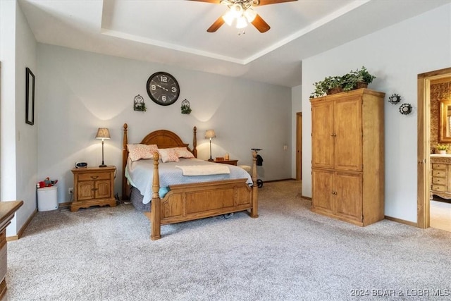 carpeted bedroom with a raised ceiling, connected bathroom, and ceiling fan