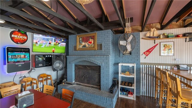 living room featuring vaulted ceiling with beams, brick wall, a brick fireplace, and wood-type flooring