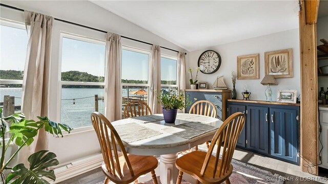 dining room with light hardwood / wood-style flooring, a water view, and vaulted ceiling