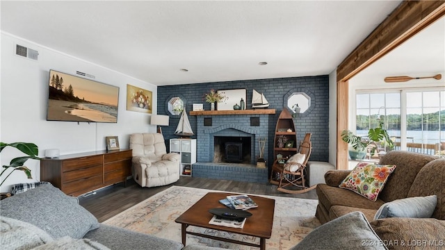 living room featuring a water view, brick wall, dark hardwood / wood-style flooring, and a brick fireplace