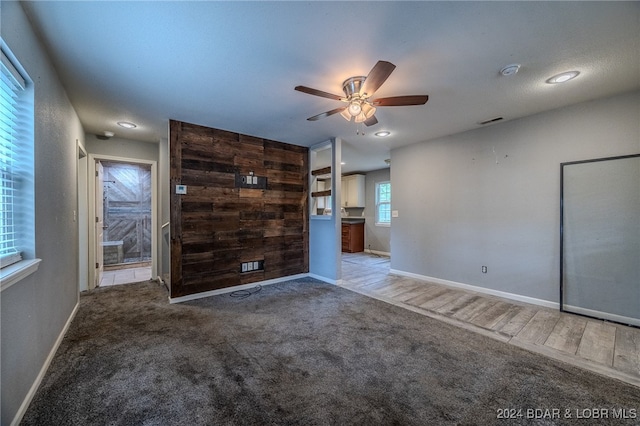 unfurnished bedroom with wood walls, light colored carpet, ensuite bathroom, and ceiling fan