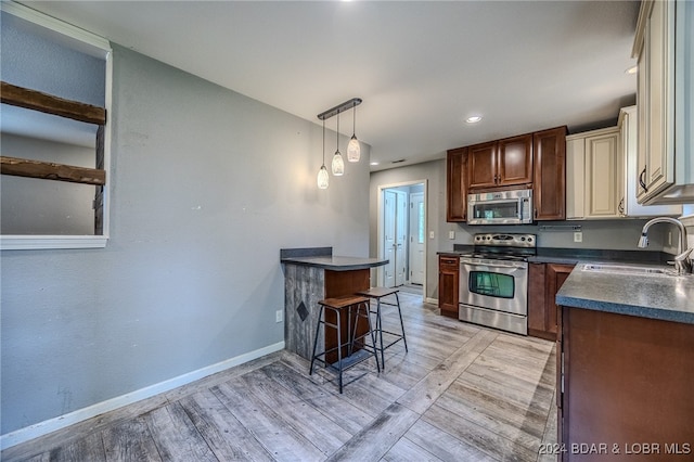 kitchen with appliances with stainless steel finishes, light wood-type flooring, sink, and a kitchen bar