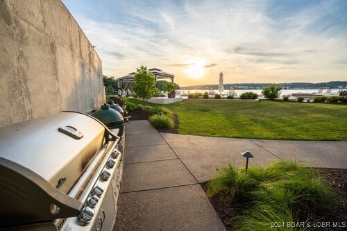 patio terrace at dusk featuring a lawn, a grill, and an outdoor kitchen