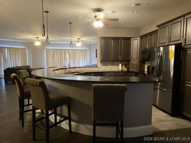 kitchen with a breakfast bar, tasteful backsplash, stainless steel refrigerator with ice dispenser, ceiling fan, and sink