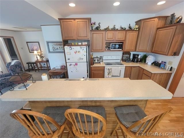 kitchen featuring light colored carpet, white appliances, and a breakfast bar