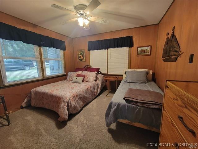 bedroom featuring wood walls, carpet, and a ceiling fan