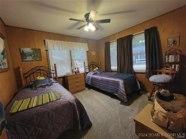 carpeted bedroom with wooden walls and ceiling fan