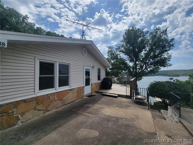 view of property exterior with a patio area, stone siding, and a deck with water view