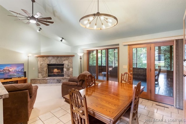 dining area featuring french doors, lofted ceiling, ceiling fan with notable chandelier, light tile patterned floors, and a stone fireplace